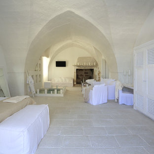 Modelo de dormitorio principal, mediterráneo, extra grande, con paredes blancas, suelo de piedra caliza, chimenea tradicional y marco de chimenea de piedra