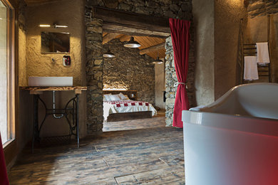Imagen de dormitorio principal rural grande con paredes multicolor, suelo de madera oscura, chimenea lineal, marco de chimenea de yeso y suelo marrón