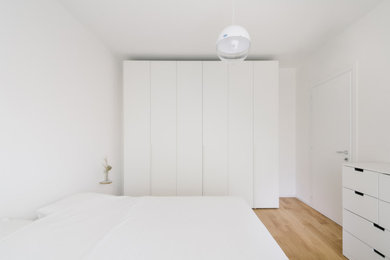 Immagine di una camera matrimoniale contemporanea di medie dimensioni con pareti bianche, parquet chiaro e pavimento marrone