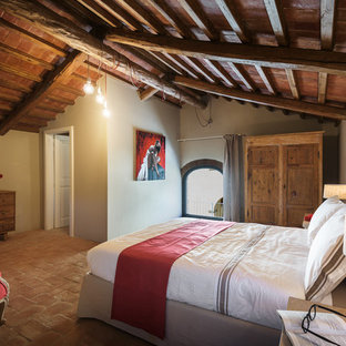 Ejemplo de dormitorio principal, de estilo de casa de campo, grande, sin chimenea, con paredes beige, suelo de baldosas de terracota y suelo rojo