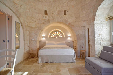Immagine di una camera matrimoniale stile rurale con pareti beige, pavimento in pietra calcarea, pavimento beige e soffitto a volta