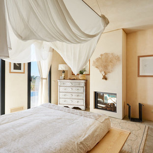Foto di una camera matrimoniale tropicale con pareti beige, pavimento in cemento, camino classico e pavimento grigio