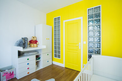 Modelo de habitación de bebé neutra clásica renovada pequeña con paredes amarillas y suelo de madera en tonos medios