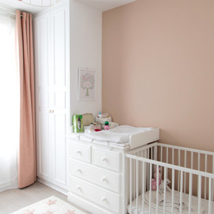 Diseño de habitación de bebé niña tradicional renovada, de tamaño medio, con paredes rosas y suelo de madera clara
