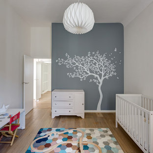Cette image montre une chambre de bébé neutre nordique de taille moyenne avec un mur gris, un sol en bois brun et un sol marron.