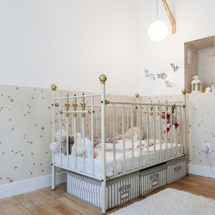Cette image montre une chambre de bébé neutre nordique de taille moyenne avec un mur blanc et un sol en bois brun.