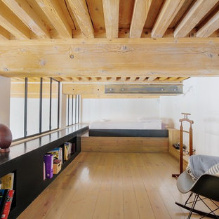 Cette image montre une chambre mansardée ou avec mezzanine urbaine avec un mur blanc, un sol en bois clair, aucune cheminée et un sol beige.