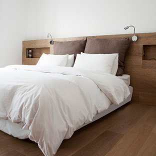 Modelo de dormitorio principal, moderno, de tamaño medio, con paredes blancas y suelo de madera en tonos medios