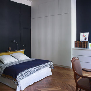 Idée de décoration pour une grand chambre parentale design avec un mur bleu et un sol en bois brun.