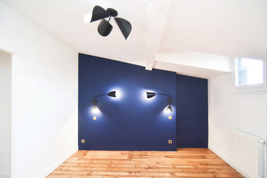 Exemple d'une grande chambre parentale tendance avec un mur bleu, parquet clair et un sol noir.