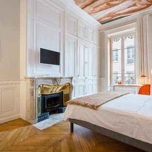 Photo of an eclectic master bedroom in Lyon with white walls, medium hardwood floors, a standard fireplace and brown floor.