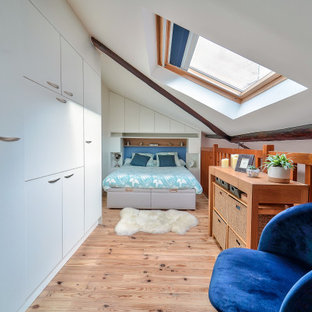 Cette photo montre une chambre mansardée ou avec mezzanine tendance avec un mur blanc, un sol en bois clair, un sol beige et un plafond voûté.
