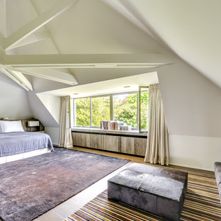 Aménagement d'une grand chambre mansardée ou avec mezzanine classique avec un mur blanc, un sol en bois clair et aucune cheminée.