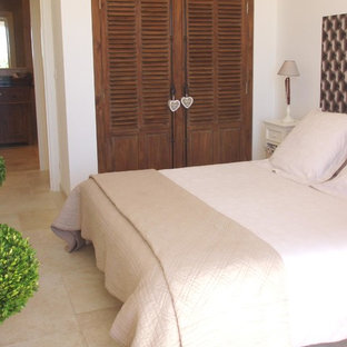 Ejemplo de dormitorio principal, mediterráneo, de tamaño medio, con paredes blancas, suelo de baldosas de cerámica, marco de chimenea de madera y suelo beige