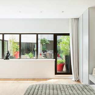Idée de décoration pour une grand chambre parentale design avec un mur blanc et un sol en bois clair.