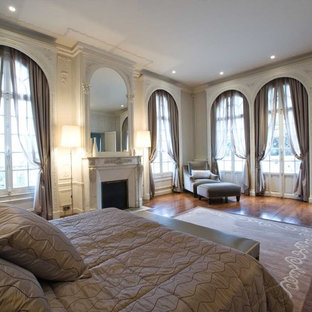 Exemple d'une très grand chambre parentale chic avec un mur beige, un sol en bois foncé, une cheminée standard et un manteau de cheminée en plâtre.