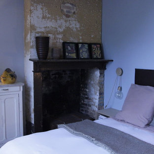 Modelo de habitación de invitados de estilo de casa de campo, de tamaño medio, con paredes azules, suelo de baldosas de terracota, chimenea tradicional y marco de chimenea de madera