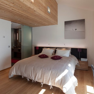 Cette photo montre une chambre parentale tendance de taille moyenne avec un mur blanc et un sol en bois brun.