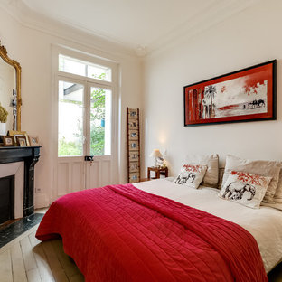 Cette photo montre une chambre parentale éclectique avec un mur blanc, une cheminée d'angle, un sol en bois peint et un manteau de cheminée en pierre.