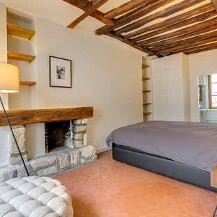 Ejemplo de dormitorio tipo loft, clásico renovado, de tamaño medio, con paredes beige, suelo de baldosas de terracota, chimenea tradicional, marco de chimenea de piedra y suelo rojo