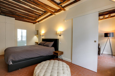 Cette photo montre une chambre mansardée ou avec mezzanine chic de taille moyenne avec un mur beige, tomettes au sol, une cheminée standard, un manteau de cheminée en pierre et un sol rouge.
