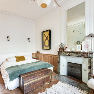 Aménagement d'une grand chambre parentale éclectique avec un mur blanc, un sol en bois brun, une cheminée standard et un manteau de cheminée en pierre.
