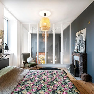 Cette image montre une grand chambre parentale design avec un mur gris, un sol en bois brun, une cheminée standard et un manteau de cheminée en pierre.