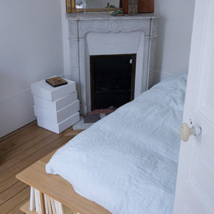 Ejemplo de dormitorio principal, contemporáneo, de tamaño medio, con paredes blancas, suelo de madera clara, chimenea de esquina y marco de chimenea de piedra