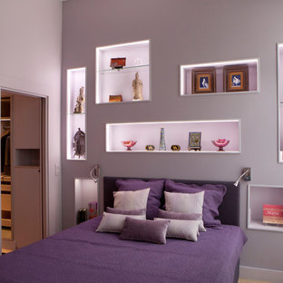 Cette photo montre une grand chambre parentale tendance avec un mur violet, un sol en bois clair, aucune cheminée et un sol marron.