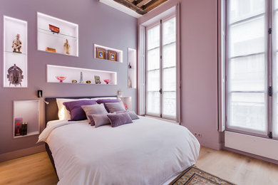 Cette photo montre une grande chambre parentale tendance avec un mur violet, parquet clair, aucune cheminée et un sol marron.