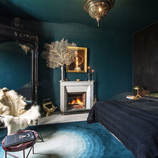 Modelo de dormitorio bohemio con paredes azules, suelo de madera pintada, chimenea tradicional, marco de chimenea de piedra y suelo blanco