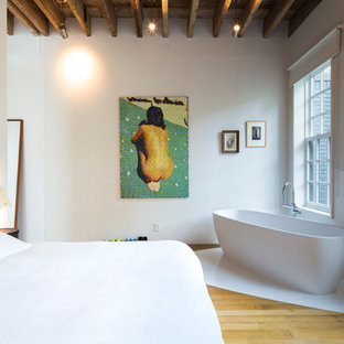 Cette photo montre une grand chambre parentale tendance avec un mur blanc et un sol en bois clair.