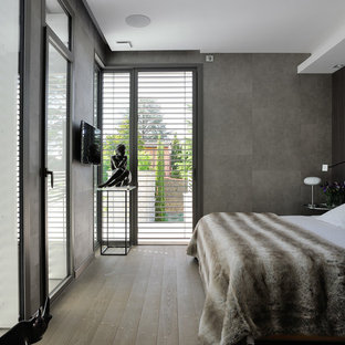 Cette photo montre une chambre parentale tendance de taille moyenne avec un mur gris et un sol en bois brun.