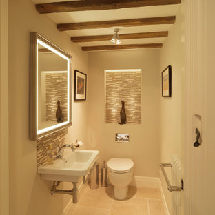 Photo of a small rural cloakroom in Hampshire with a wall-mounted sink, beige walls, a one-piece toilet, beige tiles, glass tiles and limestone flooring.