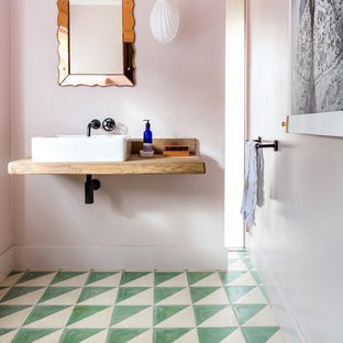 Bild på ett stort eklektiskt brun brunt toalett, med rosa väggar, cementgolv, ett väggmonterat handfat, träbänkskiva och grönt golv