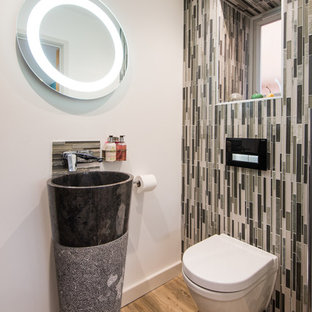Inspiration for a small modern cloakroom in West Midlands with a wall mounted toilet, multi-coloured tiles, matchstick tiles, beige walls, medium hardwood flooring, a pedestal sink and brown floors.