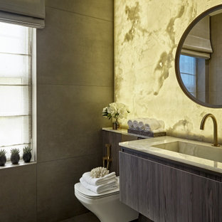 Photo of a contemporary cloakroom in London with flat-panel cabinets, grey cabinets, a wall mounted toilet, grey tiles, grey walls, an integrated sink, grey floors, white worktops and a floating vanity unit.
