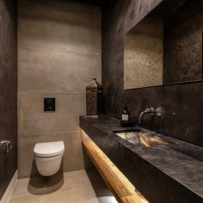 Mid-sized tuscan concrete floor and gray floor powder room photo in West Midlands with a wall-mount toilet, black walls and a wall-mount sink