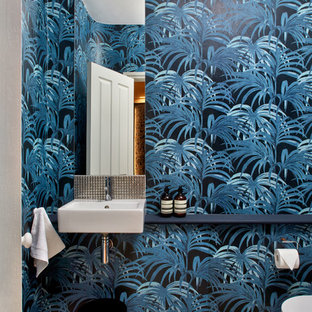 This is an example of a small contemporary cloakroom in London with a wall mounted toilet, blue walls, light hardwood flooring, open cabinets, a wall-mounted sink, wooden worktops, beige floors and blue worktops.