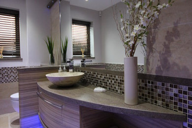 Photo of a small contemporary cloakroom in Other with a vessel sink, flat-panel cabinets, medium wood cabinets, solid surface worktops, a wall mounted toilet, multi-coloured tiles, mosaic tiles and travertine flooring.