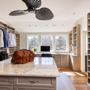 Modelo de armario vestidor unisex, de estilo de casa de campo, grande, con armarios abiertos, puertas de armario de madera clara, suelo de madera en tonos medios y suelo marrón