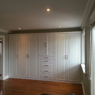 Imagen de armario unisex, clásico, grande, con armarios con paneles con relieve, puertas de armario blancas y suelo de madera en tonos medios