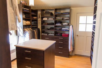 Modelo de armario vestidor unisex clásico grande con puertas de armario de madera en tonos medios, suelo de madera clara y armarios abiertos