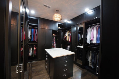 Diseño de armario vestidor unisex actual grande con armarios estilo shaker, puertas de armario negras, suelo de madera oscura y suelo marrón