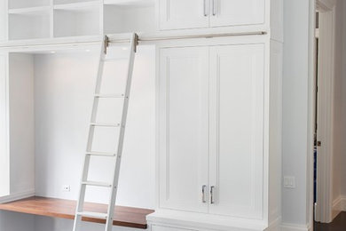 Modelo de armario vestidor unisex tradicional renovado de tamaño medio con armarios con paneles empotrados, puertas de armario blancas y suelo de madera oscura