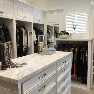 Aménagement d'un grand dressing bord de mer neutre avec un placard avec porte à panneau surélevé, des portes de placard blanches, moquette et un sol beige.