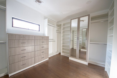 Modelo de armario vestidor unisex actual de tamaño medio con armarios con paneles lisos, puertas de armario de madera clara y suelo de madera en tonos medios