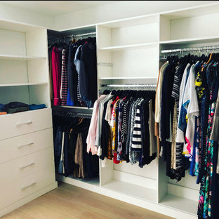 Ejemplo de armario vestidor de mujer, actual, de tamaño medio, con armarios con paneles lisos, puertas de armario blancas, suelo laminado y suelo marrón