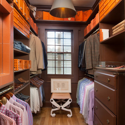 Elegant men's medium tone wood floor walk-in closet photo in New Orleans with open cabinets and dark wood cabinets