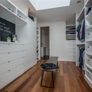Imagen de armario vestidor unisex, actual, grande, con armarios con paneles lisos, puertas de armario blancas, suelo de madera en tonos medios y suelo marrón